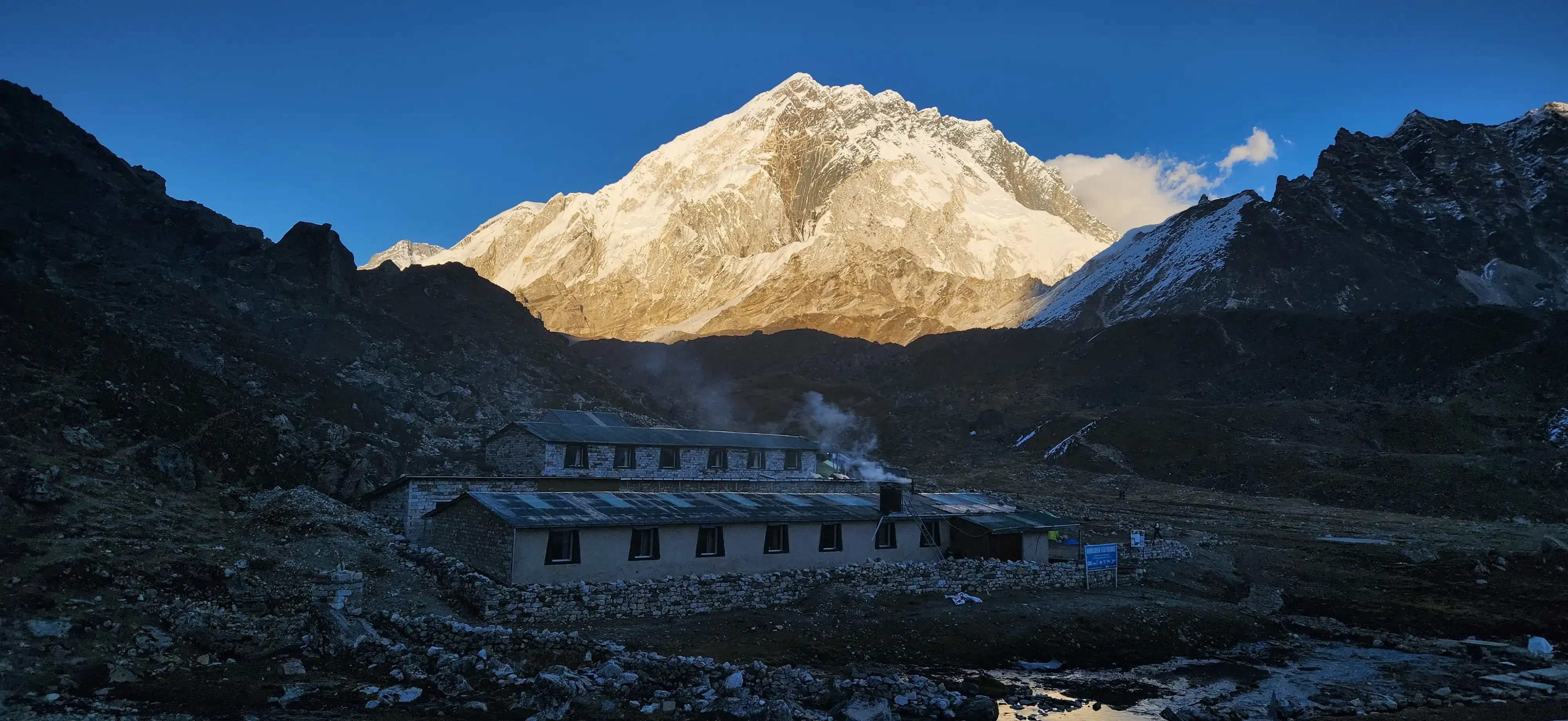 A lodge in Lobuche with a mountain painted in golden hue at sunset.